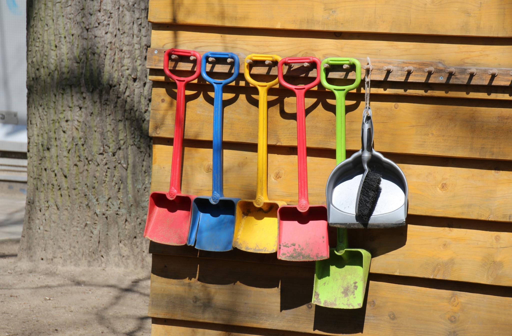 Bunte Kinderschaufeln hängen an einer Holzwand.