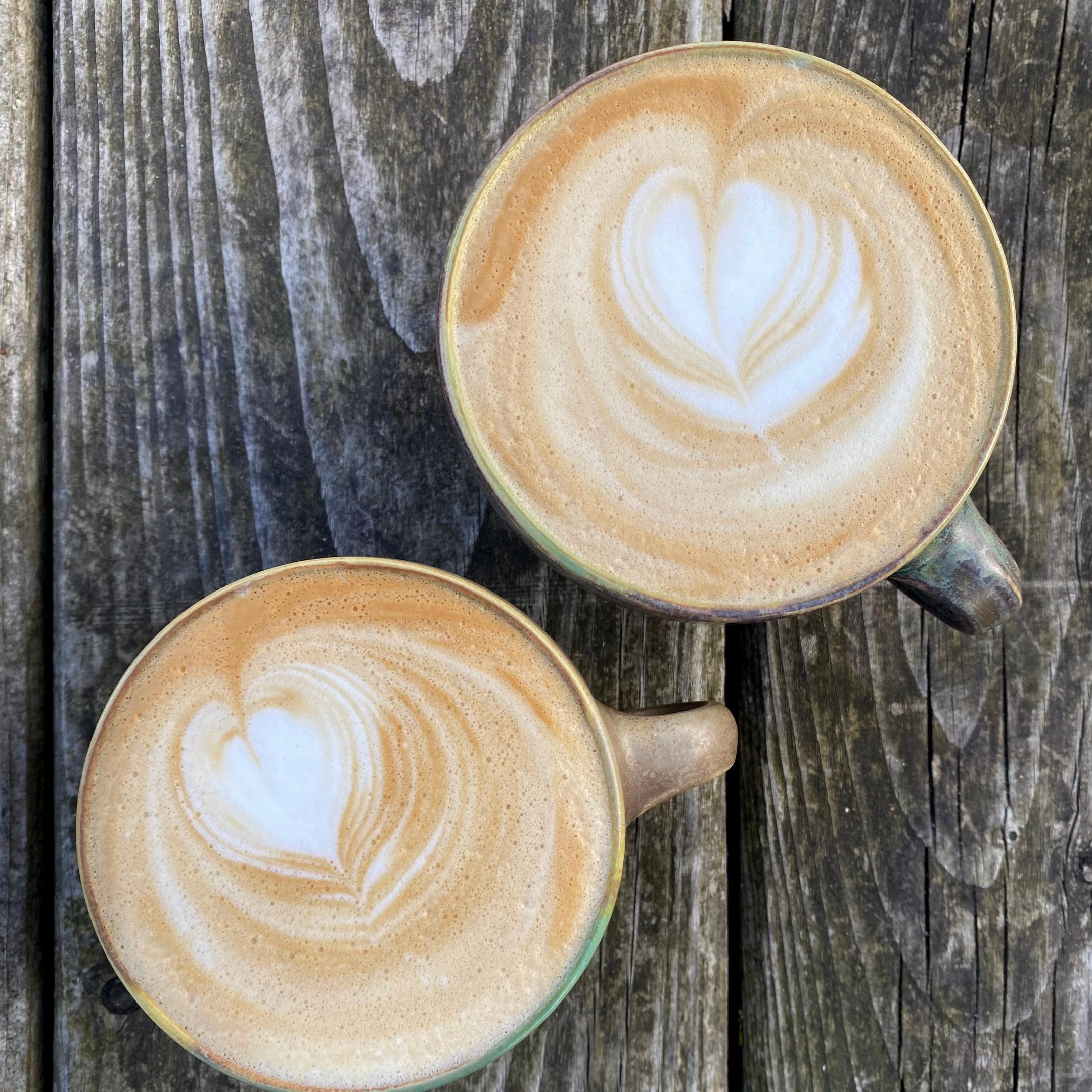 Zwei Kaffeetassen. Der Milchschaum bildet ein Herz-Muster.